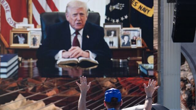 Uma pessoa adora enquanto uma mensagem de vídeo gravada do presidente Donald Trump é reproduzida no Rededicate 250. 
