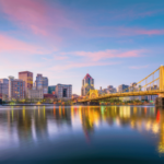 Horizonte de Pittsburgh ao pôr do sol com pontes amarelas iluminadas refletindo sobre o rio Allegheny, no centro da Pensilvânia. Reguladores da Pensilvânia aprovam US$ 180 mil em multas de jogos enquanto expandem listas de exclusão involuntária