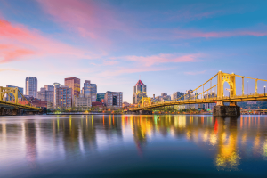 Reguladores da Pensilvânia aprovam US$ 180 mil em multas de Horizonte de Pittsburgh ao pôr do sol com pontes amarelas iluminadas refletindo sobre o rio Allegheny, no centro da Pensilvânia. Reguladores da Pensilvânia aprovam US$ 180 mil em multas de jogos enquanto expandem listas de exclusão involuntária