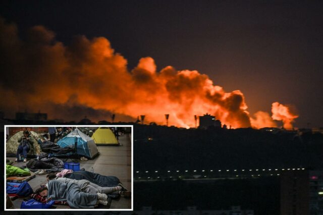 Rússia ataca Kyiv com mísseis balísticos após promessa de “punir” Vista noturna do horizonte de uma cidade com grandes nuvens de fumaça laranja subindo para o céu por trás dos edifícios.