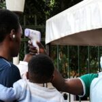 Uma autoridade de saúde usa um termômetro para examinar as pessoas em frente ao Hospital Muçulmano Kibuli, em Kampala, Uganda.