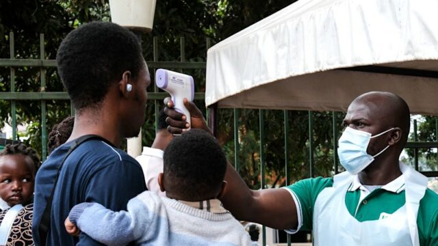 Uma autoridade de saúde usa um termômetro para examinar as pessoas em frente ao Hospital Muçulmano Kibuli, em Kampala, Uganda.