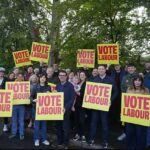 Burnham em Makerfield com ativistas trabalhistas, incluindo Lucy Powell e Liam Conlon (primeira fila, segurando o segundo cartaz da direita) em uma foto que os dois últimos postaram no X
