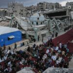 Uma menina segurando um doce entre os palestinos realizando as orações matinais marcando o início do Eid al-Adha, a Festa do Sacrifício, em uma rua fortemente danificada em Khan Yunis, no sul da Faixa de Gaza, em 27 de maio de 2026.