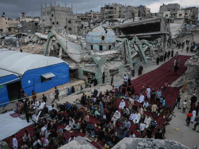 Uma menina segurando um doce entre os palestinos realizando as orações matinais marcando o início do Eid al-Adha, a Festa do Sacrifício, em uma rua fortemente danificada em Khan Yunis, no sul da Faixa de Gaza, em 27 de maio de 2026.