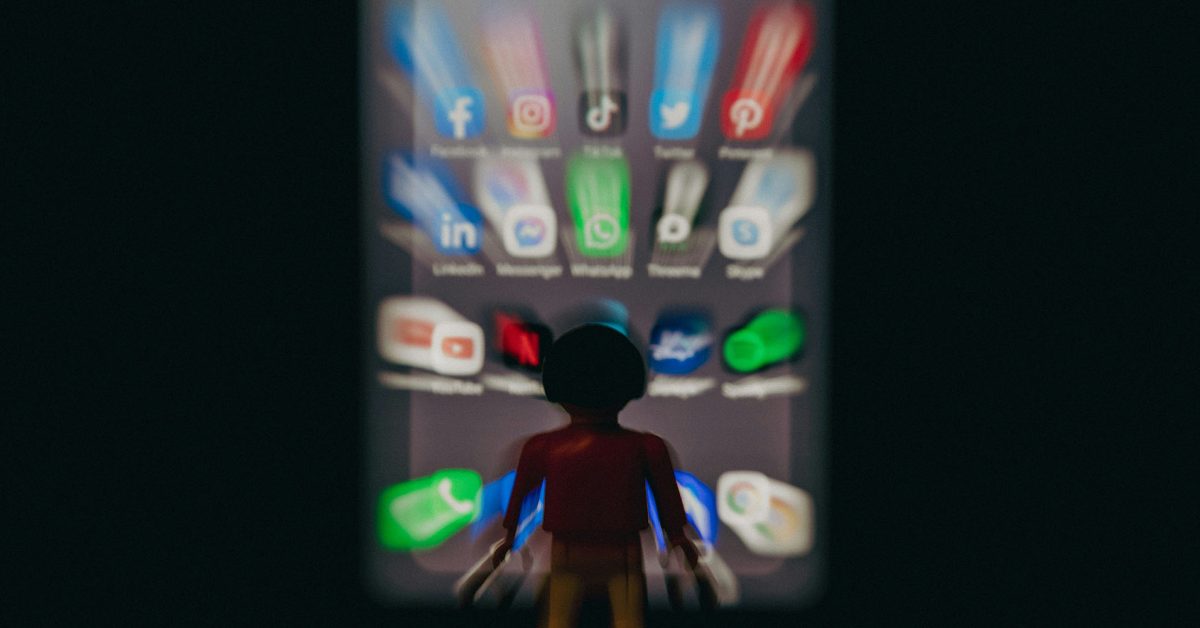 60% dos vídeos do TikTok são resíduos de IA; 21% dos do YouTube | A imagem mostra um personagem robô de brinquedo em frente a um conjunto desfocado de ícones de aplicativos