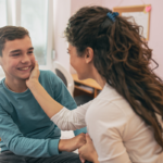 Stock photo: A happy mother touching and cuddling her teenage son on the face in his bedroom.