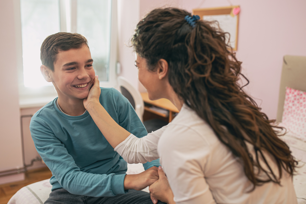 Stock photo: A happy mother touching and cuddling her teenage son on the face in his bedroom.