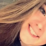 Selfie de Emily Moore. Ela está sorrindo para a câmera. Ela tem longos cabelos castanhos. A foto é tirada em um ângulo de forma que o topo de sua cabeça fique no canto superior direito, enquanto seu cabelo cai para baixo. Ela parece genuinamente feliz.