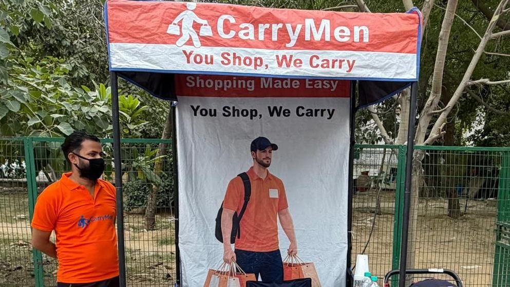 Os fundadores Ritu Kandari Srivastava (em sari verde) e Kanishka Malhotra (em calças pretas e blusa vermelha) no quiosque CarryMen no mercado Lajpat Nagar