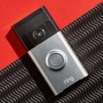 Ring video camera doorbell on a red plain and black textured background.