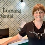 Criança com a boca aberta enquanto as mãos enluvadas aplicam algo nos dentes.
