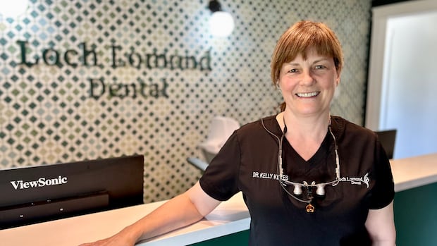 Criança com a boca aberta enquanto as mãos enluvadas aplicam algo nos dentes.