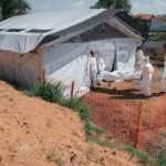 Jospin Mwisha/AFP via Getty Images - FOTO: Membros de equipes de resposta especializadas entram no necrotério do Centro Médico Evangélico de Nyankunde com o corpo de uma pessoa que morreu da doença do vírus Ebola em Bunia, província de Ituri, República Democrática do Congo, em 13 de junho de 2026.