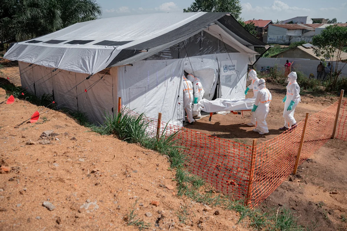 Jospin Mwisha/AFP via Getty Images - FOTO: Membros de equipes de resposta especializadas entram no necrotério do Centro Médico Evangélico de Nyankunde com o corpo de uma pessoa que morreu da doença do vírus Ebola em Bunia, província de Ituri, República Democrática do Congo, em 13 de junho de 2026.