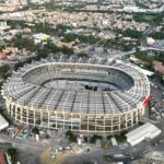 Pessoas caminham perto da estátua caída de um jogador de futebol