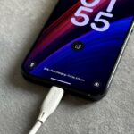 Uma mão segurando um smartphone com um ícone de bateria fraca no centro.