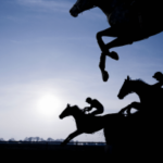 Jóqueis em silhueta montam cavalos de corrida em um salto com obstáculos durante um evento de corrida de cavalos, ilustrando corridas de puro-sangue e esporte equestre contra um céu dramático. Credores de Hawthorne buscam investigação sobre fundos de corrida em meio a um caso de disputa de falência