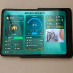 Tablet Android exibindo controles de casa inteligente em uma mesa ao lado de um pequeno vaso de planta.