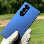 Samsung Galaxy Z Fold 7, com um dispositivo em pé e outro parcialmente dobrado, contra um fundo vermelho e bege