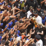 Jalen Brunson, no canto superior direito, do campeão da NBA New York Knicks carrega o troféu para os fãs durante o desfile na Broadway, em Nova York