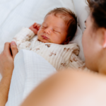 Close-up of newborn baby peacefully sleeping next to mother, wrapped in a soft white blanket.