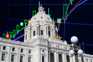 Edifício do Capitólio do Estado de Minnesota em St. Paul com gráficos do mercado financeiro e castiçais de negociação sobrepostos, ilustrando a batalha legal de Minnesota sobre os mercados de previsão, Kalshi, Polymarket e a proibição criminal do estado de apostas baseadas em eventos. Minnesota luta contra os desafios da legislação de mercado de previsão