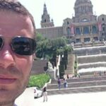 Um policial se inclina ao lado de uma cerca de metal que está atrás de fita policial