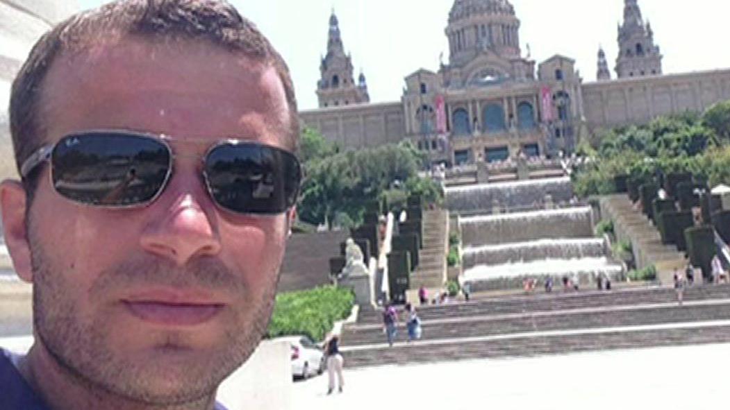 Um policial se inclina ao lado de uma cerca de metal que está atrás de fita policial