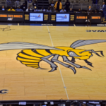 Visão ampla da quadra de basquete do Alabama State Hornets com o grande logotipo do hornet na quadra central, ligada às descobertas da NCAA envolvendo ex-jogadores do estado do Alabama na investigação de manipulação de apostas no sul do Mississippi.