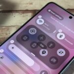 Uma ilustração fotográfica de uma pessoa segurando um Samsung Galaxy Z Flip 6 contra um fundo rosa e amarelo