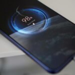 Uma mão segurando um smartphone com um ícone de bateria fraca no centro.