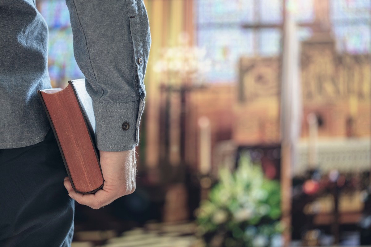 Stock image of a man holding a Bible with a church altar in the background.