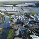 O sol pode ser visto atrás de uma bomba eólica do século 20 em Norfolk Broads, com uma nova estação de bombeamento elétrica visível em primeiro plano