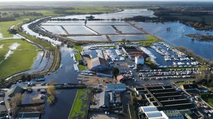 O sol pode ser visto atrás de uma bomba eólica do século 20 em Norfolk Broads, com uma nova estação de bombeamento elétrica visível em primeiro plano