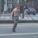 Um homem de peito nu carregando o que parece ser uma faca grande em uma rua