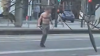 Um homem de peito nu carregando o que parece ser uma faca grande em uma rua