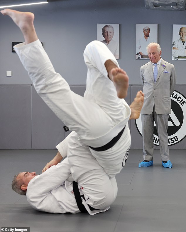 Um fascinado Rei Charles observa - usando galochas protetoras - enquanto assiste a uma partida de Jiu Jitsu durante uma visita ao oeste de Londres para saber mais sobre a instituição de caridade Reorg