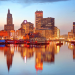 O horizonte de Rhode Island ao pôr do sol refletido no rio Providence, destacando o centro de Providence enquanto os legisladores consideram expandir o mercado de apostas esportivas do estado e acabar com seu monopólio de apostas esportivas.