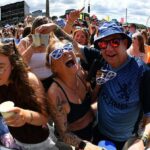 Perrie se apresenta no palco do festival TRNSMT. Ela está segurando um microfone e sorrindo, vestindo uma blusa preta e com cabelos castanhos na altura dos ombros.