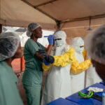 Jospin Mwisha/AFP via Getty Images - FOTO: Profissionais de saúde colocam equipamentos de proteção individual na área de curativos sob a supervisão de especialistas antes de examinarem os pacientes na enfermaria de isolamento do Centro de Tratamento de Ebola em Munigi, em 2 de junho de 2026.