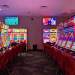 Vista interna do Two Coppers Casino em Juneau, Alasca, com fileiras de máquinas de jogos eletrônicos, cadeiras vermelhas, displays de caça-níqueis brilhantes e telas de televisão suspensas durante a inauguração do cassino.