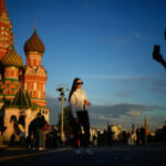 Pavel Bednyakov/AP Photo/Pavel Bednyakov - FOTO: Uma mulher posa para uma foto em frente à Catedral de São Basílio na Praça Vermelha durante o pôr do sol em Moscou, em 2 de junho de 2026.