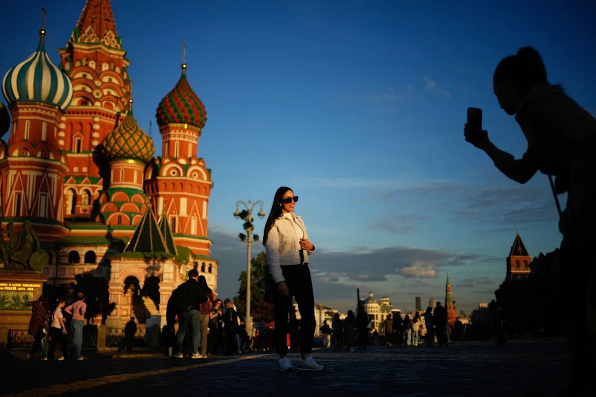 Pavel Bednyakov/AP Photo/Pavel Bednyakov - FOTO: Uma mulher posa para uma foto em frente à Catedral de São Basílio na Praça Vermelha durante o pôr do sol em Moscou, em 2 de junho de 2026.