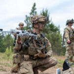 Soldados camuflados e armados com rifles caminham por uma trilha na floresta.