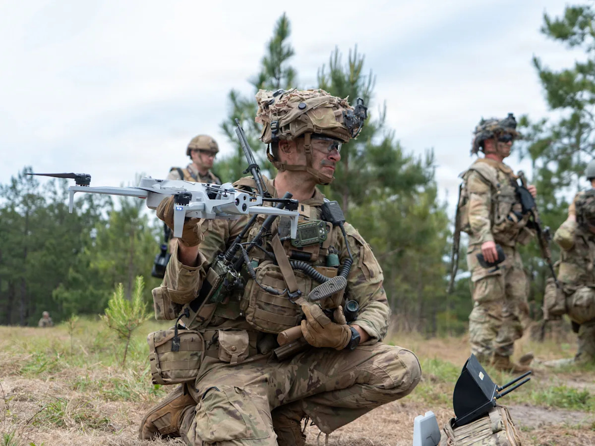 Soldados camuflados e armados com rifles caminham por uma trilha na floresta.