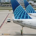 Cabine do avião United com telas nos encostos dos bancos e uma cozinha aberta para bebidas abastecida com refrigerantes e água mineral.