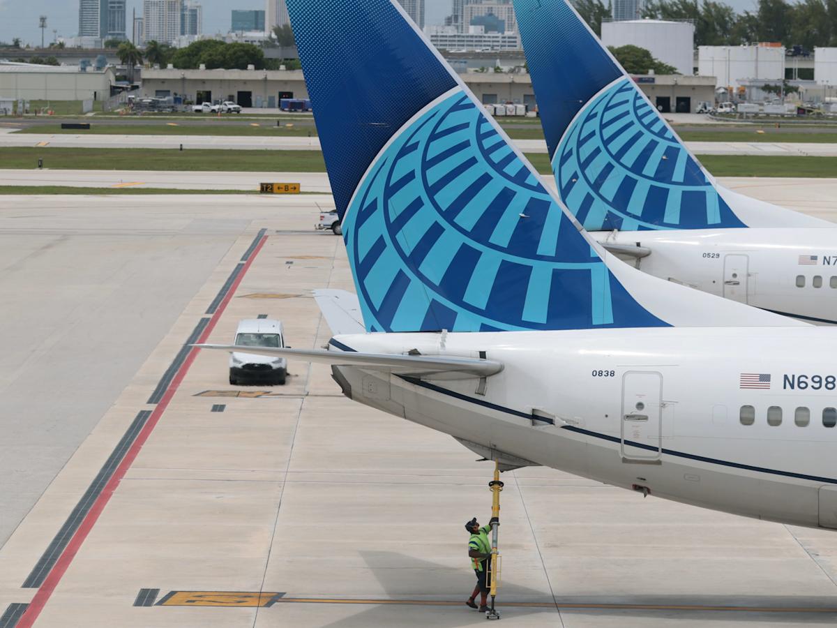 Cabine do avião United com telas nos encostos dos bancos e uma cozinha aberta para bebidas abastecida com refrigerantes e água mineral.