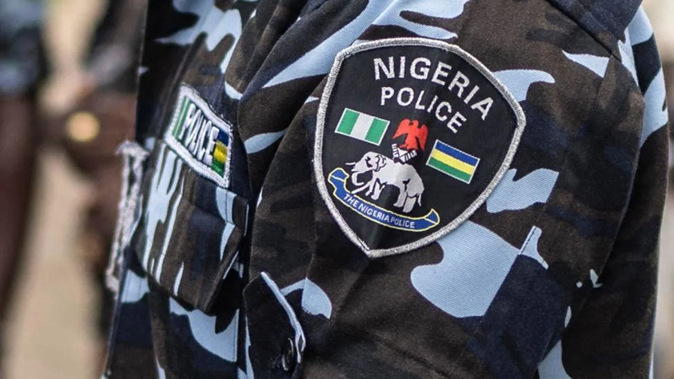 À direita do banner, uma mulher com óculos escuros na cabeça, jaqueta jeans e camiseta amarela olha para o celular. Um gráfico da BBC News Africa em preto e vermelho está à esquerda da imagem, que tem um fundo marrom dourado claro.