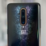 Smartphone OnePlus 16 flutuando na frente de um '16' azul brilhante, cercado por partículas de cinzas e fumaça leve.